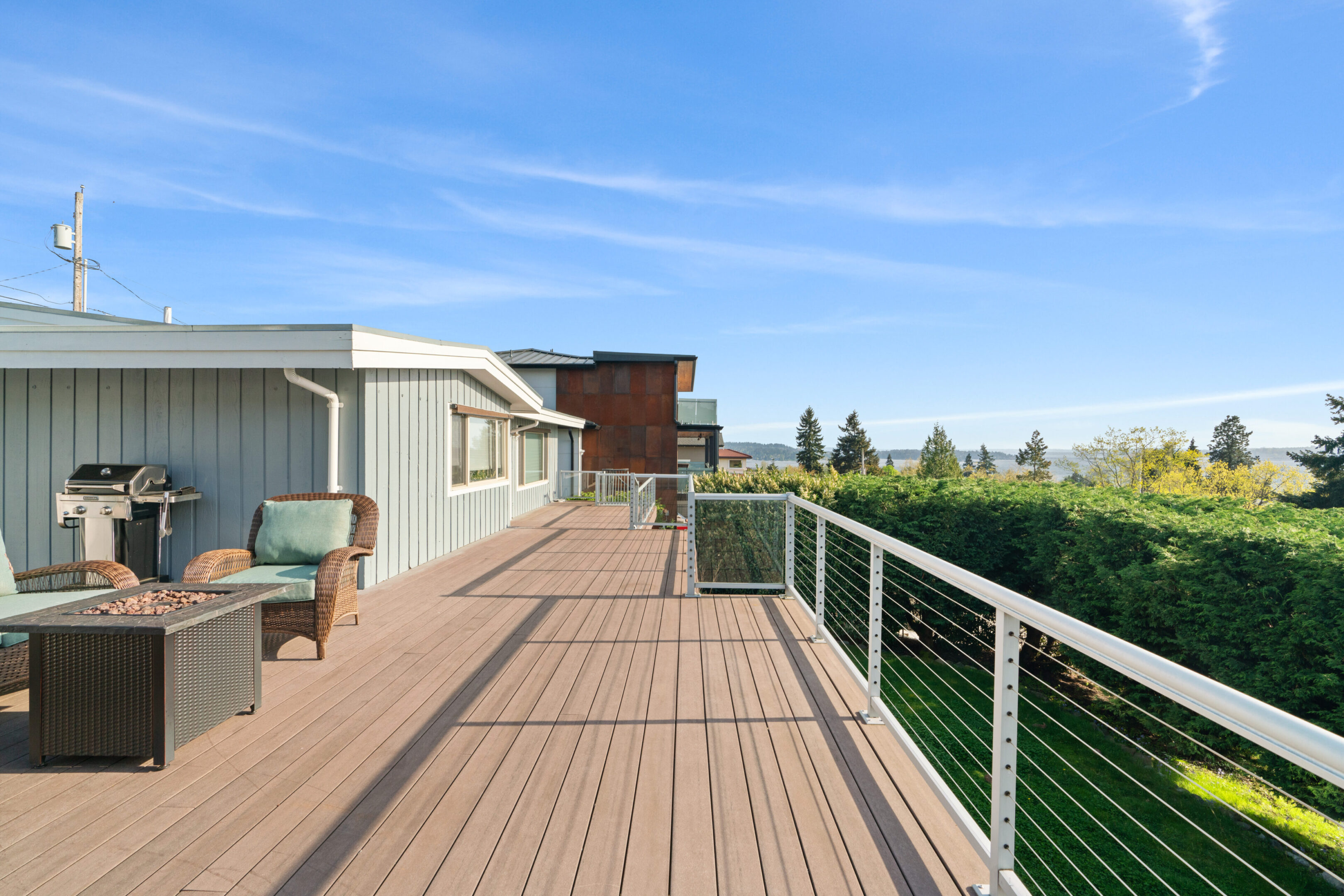 Wicker chairs surrounding a rectangular fire pit on an outdoor wooden deck with a fantastic view of Lake Washington in Kirkland.